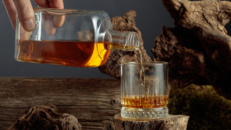 whiskey pouring from a bottle into a glass set atop a small stump