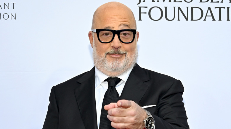 Andrew Zimmern in a black suit, pointing, in front of a James Beard Foundation backdrop