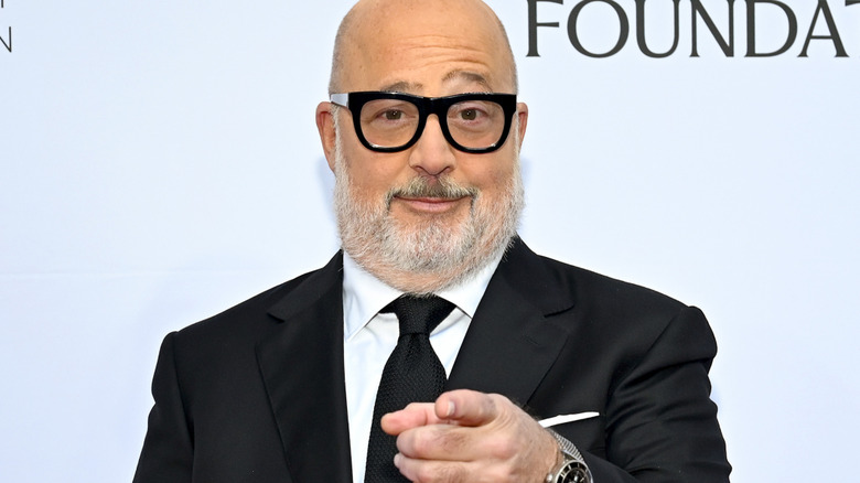 Andrew Zimmern in glasses and a suit pointing with his finger