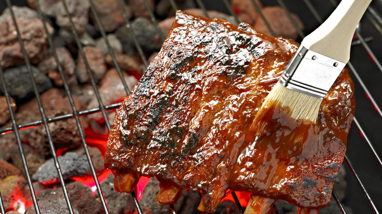 A basting brush slathers sauce onto a rack of ribs on the barbecue.