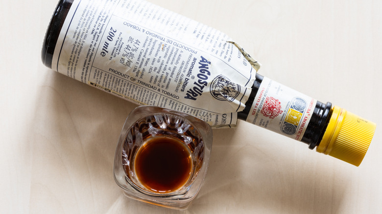 A bottle of Angostura Bitters next to a small glass with a small amount inside.