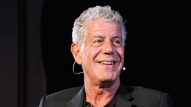 Anthony Bourdain, dressed in black, smiling with a small microphone beside his cheek