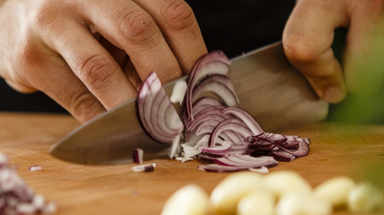 Chef slicing an onion with fingers at the proper angle and position.
