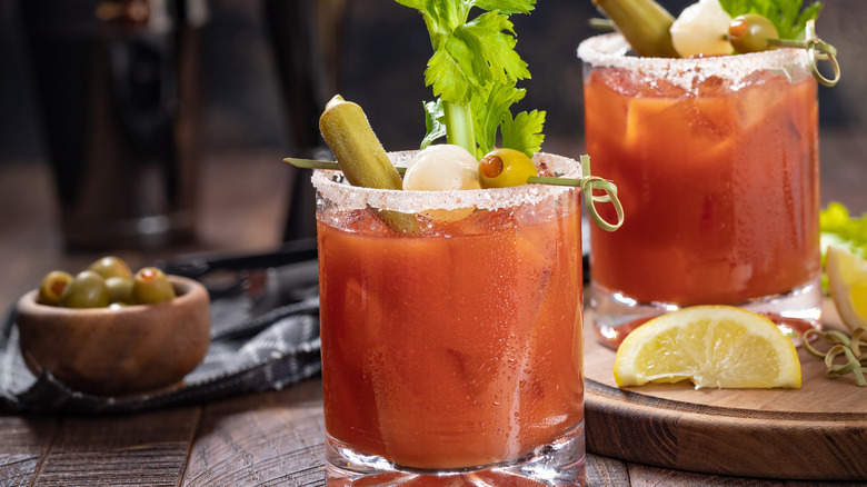 Two bloody mary cocktails in rocks glasses with garnishings.
