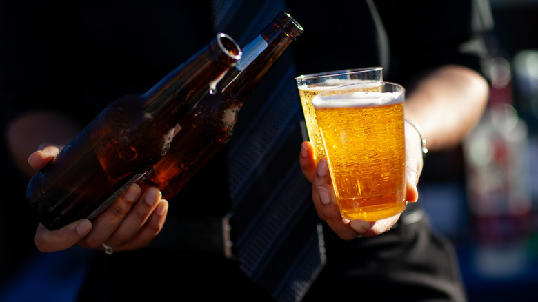 Person holding two beer bottles and two glasses