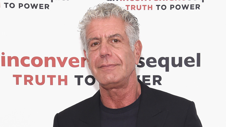 Anthony Bourdain holding up a copy of his cookbook, Appetites