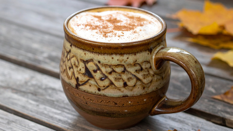 latte with cinnamon topping served in mug with autumn leaves in background