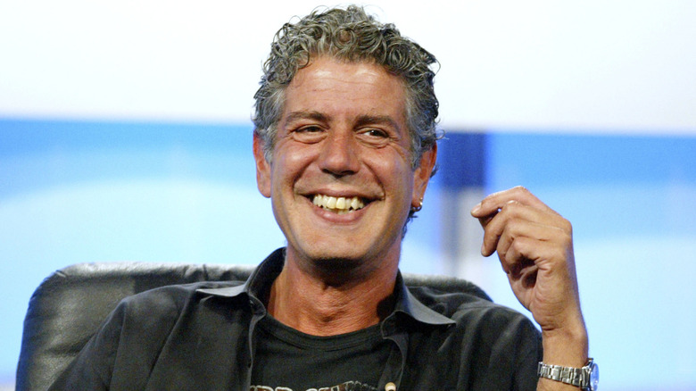 Anthony Bourdain smiling cheekily while sitting on stage