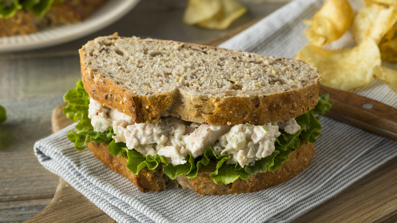 A chicken salad sandwich on a plate beside a knife and some potato chips