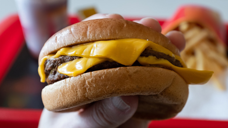 one hand holding a simple fast food cheeseburger with two patties