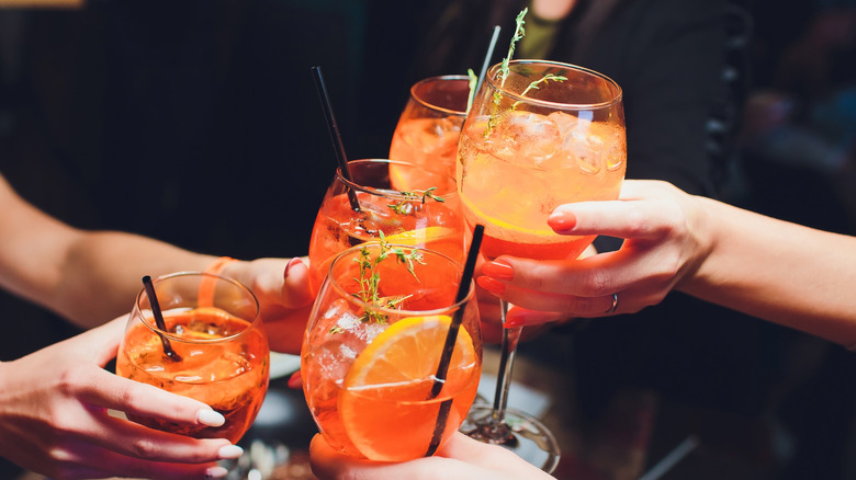 A group of people clink aperol spritzes
