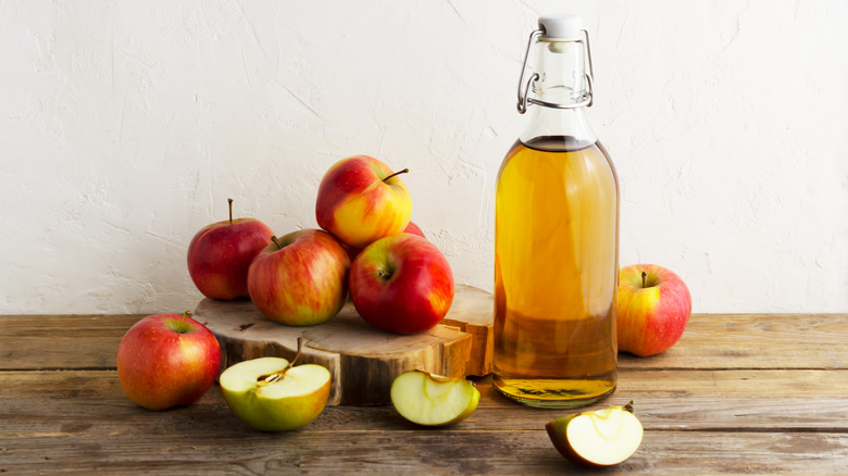whole apples behind a glass bottle of juice or cider