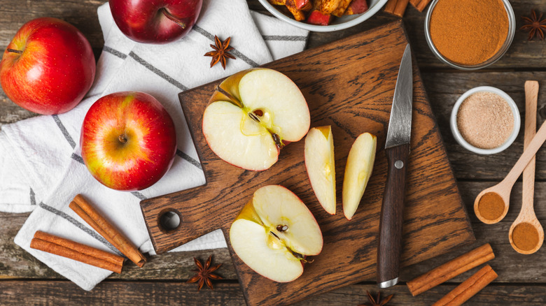 sliced apples and a paring knife on a cutting board surrounded by other apple pie ingredients