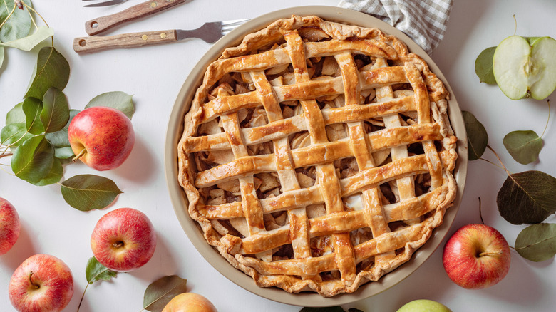 apple pie with apples on table around it