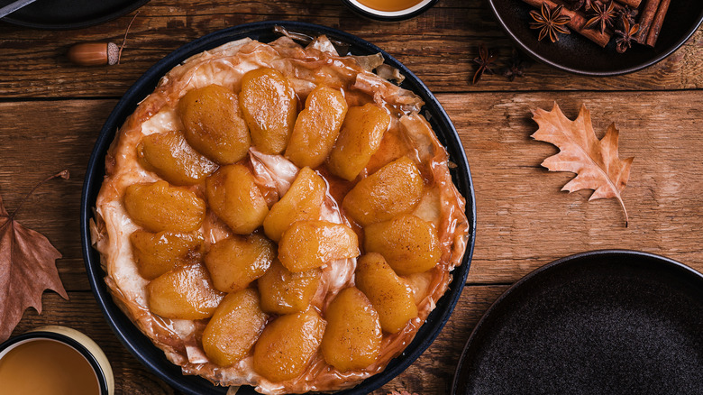 apple tarte tatin on wooden table with oak leaves, acorns, and whole spices