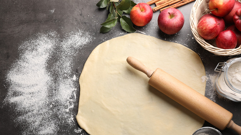 Rolled out pie crust dough on a table next to whole apples