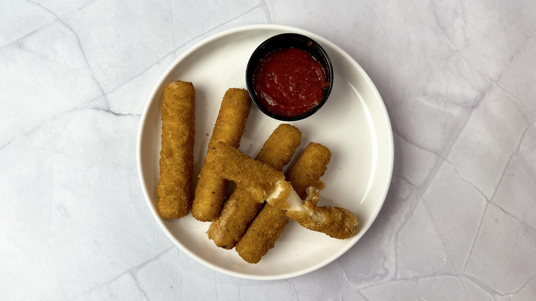 Applebee's mozzarella sticks on a white plate with cup of marinara sauce