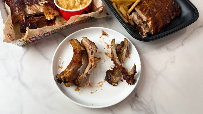 Chili's and Applebee's baby back rib bones on a white plate with takeout containers in the background