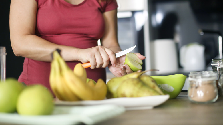 A person cuts into an apple, bananas foregrounded