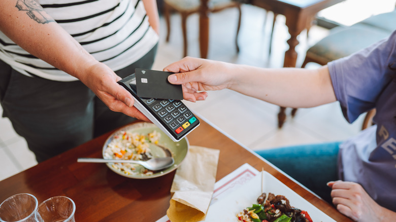 A server holds a handheld register out while a customer taps their card