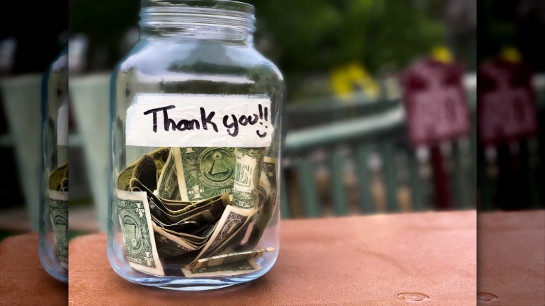 A glass tip jar full of dollars