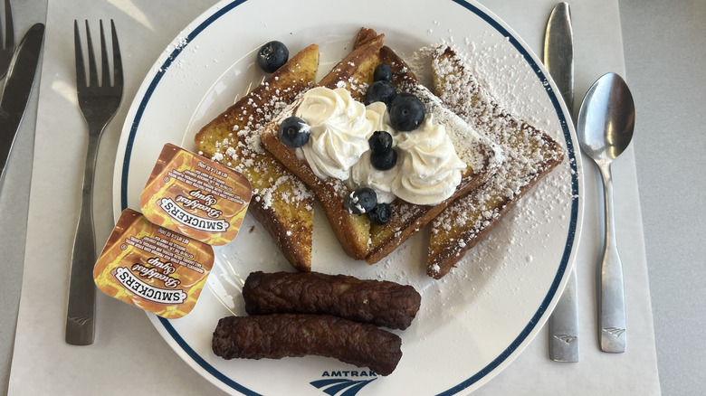 French toast with blueberries, whipped cream, and sausage on a white Amtrak plate.