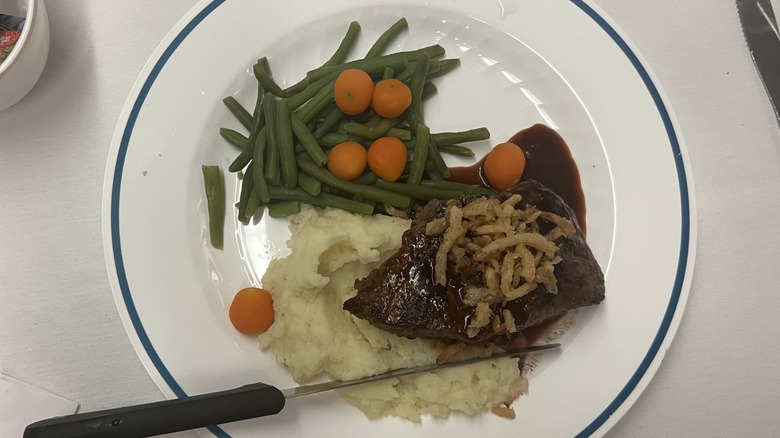 Flat-iron steak with crispy onions, mashed potatoes, and veggies on white Amtrak plate.