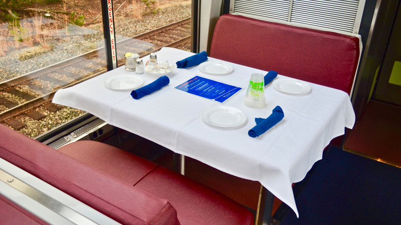Red booth in Amtrak dining car with white tablecloth and four place settings.