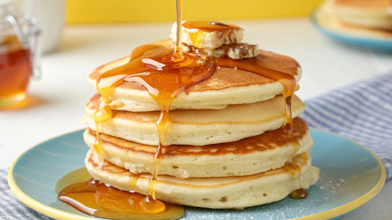 Stack of pancakes with banana and maple syrup poured on top