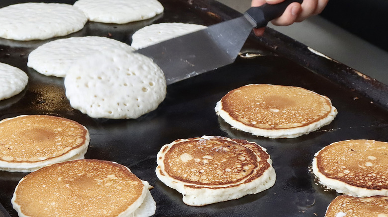 Flipping several pancakes on a large black griddle