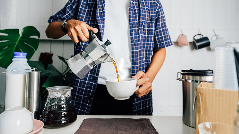 Person pouring coffee from a percolator into a mug