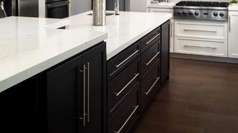 Dark kitchen cabinets on island with white granite top in kitchen.