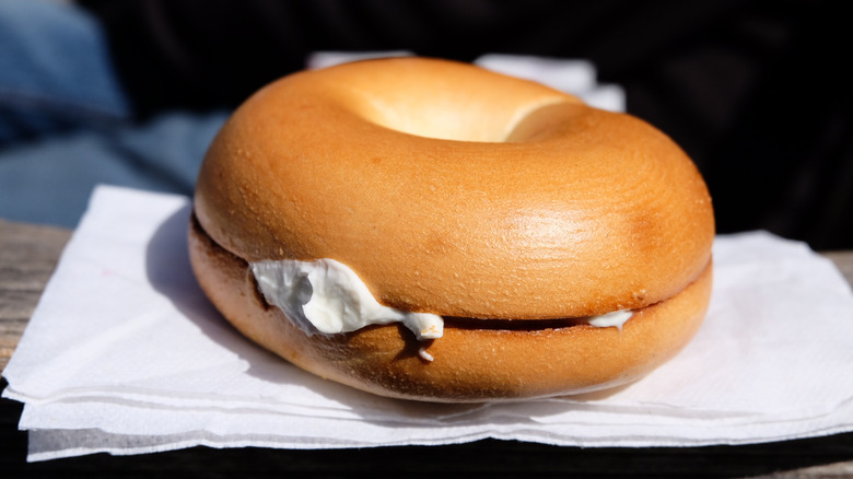 Plain bagel cut in half with cream cheese sandwiched between on white napkin