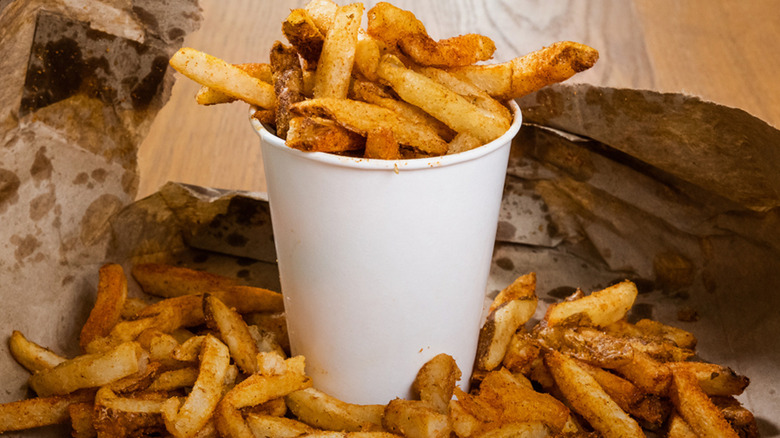 A cup of Five Guys fries spilling out onto some greasy brown paper