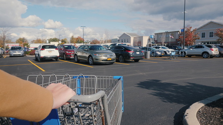 Customer pushing a shopping cart through a grocery store parking lot