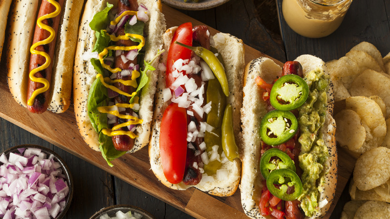 Line of hot dogs with varied toppings on wooden cutting board
