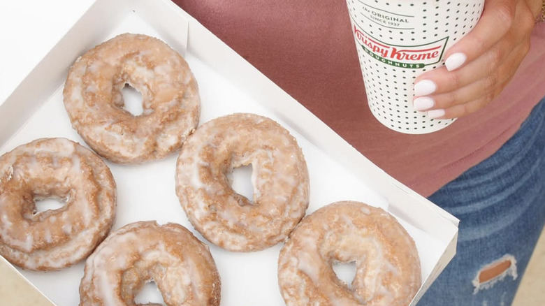 Person holding a box of Krispy Kreme cake doughnuts and a coffee cup