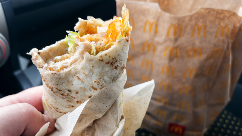 Someone holding a McDonald's Snack Wrap after taking a bite, with a paper bag in the background