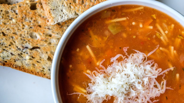 Close-up of minestrone-like soup topped with parmesan, with two toasted slices of bread in the background