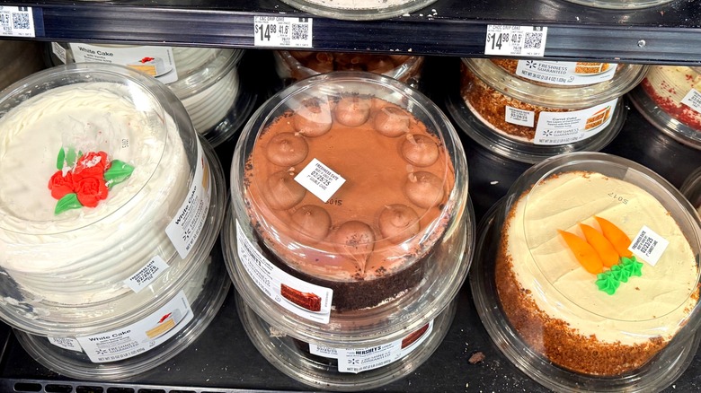 Decorated round cakes on display at Walmart including white cake with red roses, chocolate cake, and carrot cake