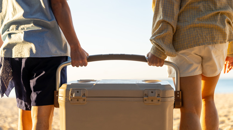 Two people carrying hard sided cooler at beach