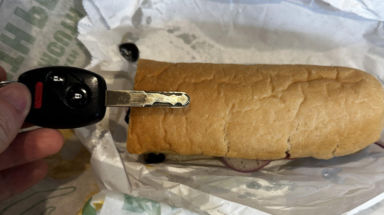 A person holds up a key in front of a subway sandwich to show size