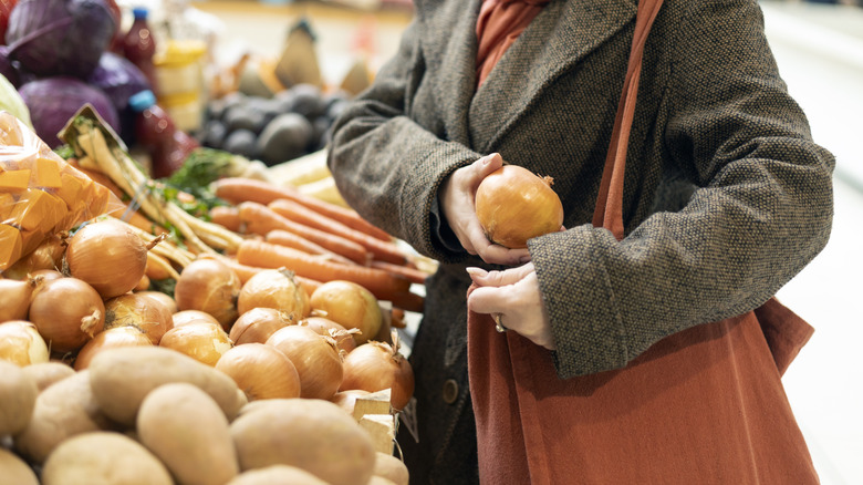 Person about to put an onion into their purse in a grocery store produce department