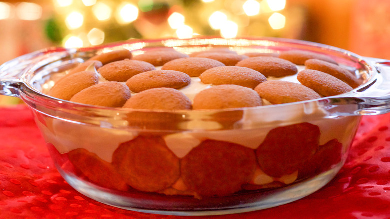 A glass bowl of banana pudding with vanilla wafers, resting on a table with soft lights in the background