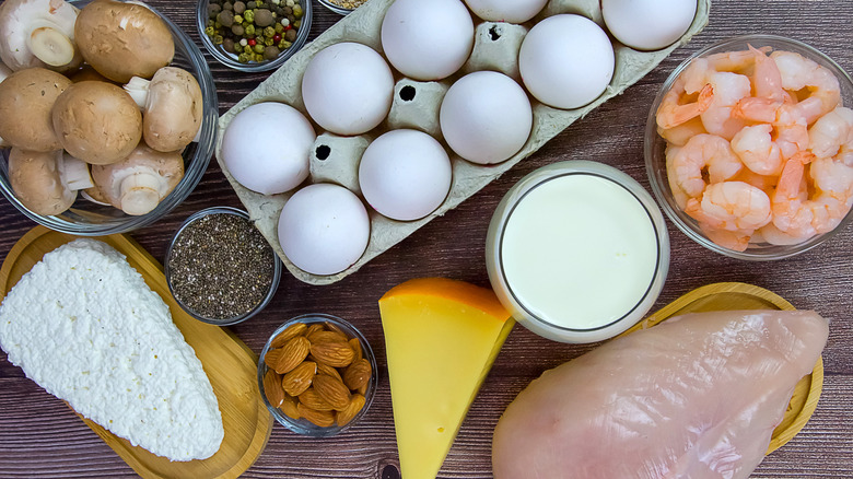 A selection of high protein foods including eggs, shrimp, cheese, nuts, chicken breast and more on a wooden table