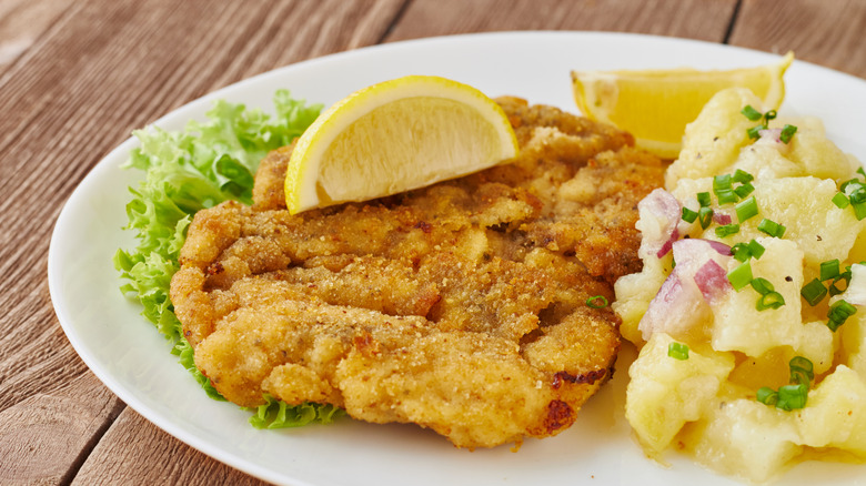 Wiener schnitzel with potato salad and lemon wedges on a white plate and wooden background