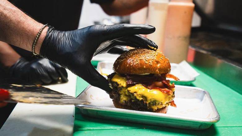 Gloved hand preparing burger on tray at Crazy Good Kitchen