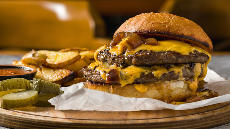 Juicy burger on parchment paper on wooden board