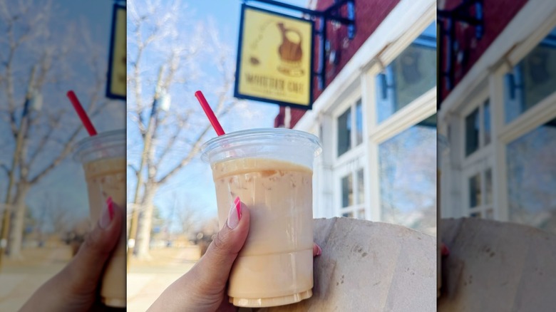 Person holding an iced latte in a plastic cup outside of Whittier Cafe in Denver