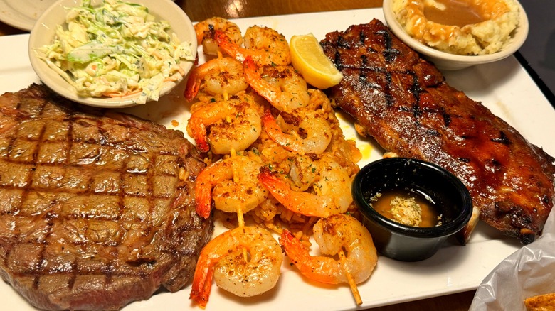 Steakhouse dishes including ribs, shrimp skewers, coleslaw, and sirloin on white rectangular plate